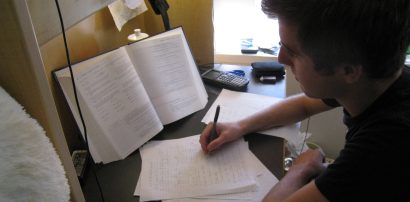 A student studying with an open textbook, taking notes at a desk
