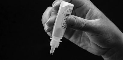 Hand holding eye drops ready to administer representing Flurbiprofen eye drop treatment